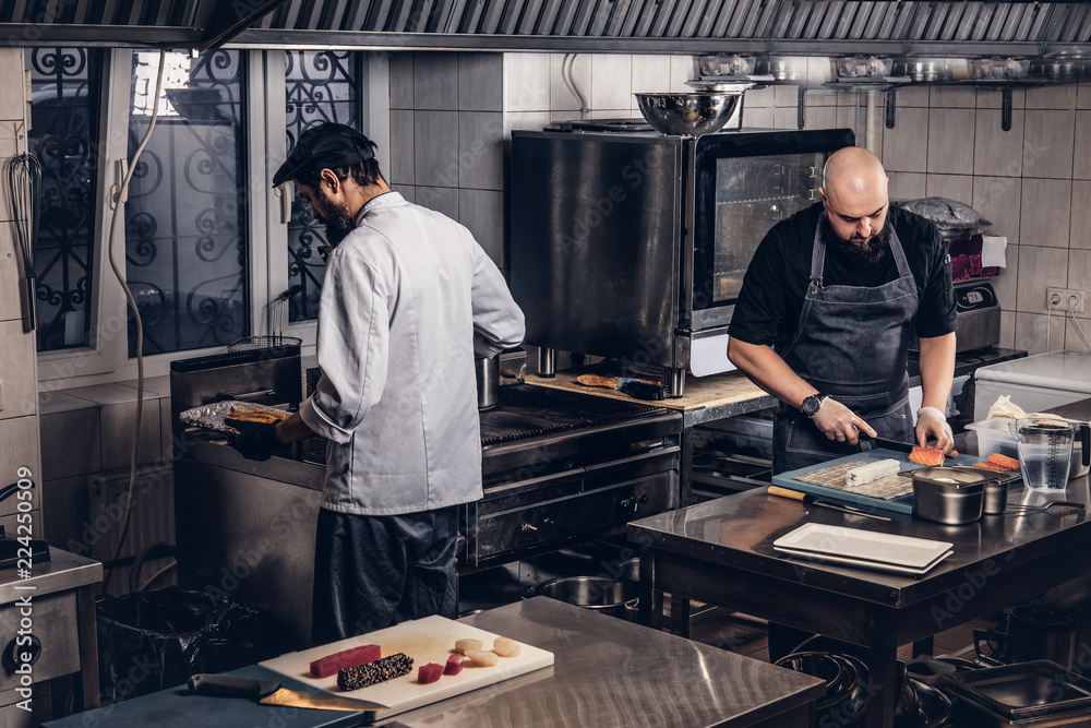 Two brutal cooks dressed in uniforms preparing sushi in a kitchen. Two brutal cooks dressed in uniforms preparing sushi in a kitchen.