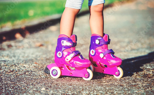 Childhood time. Little girl with roller skates in the park, close up photo