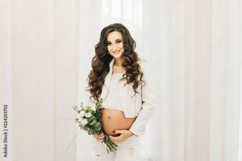 Stylish young pregnant girl in white clothes with curls and flowers. Photos waiting for baby Stylish young pregnant girl in white clothes with curls and flowers. Photos waiting for baby