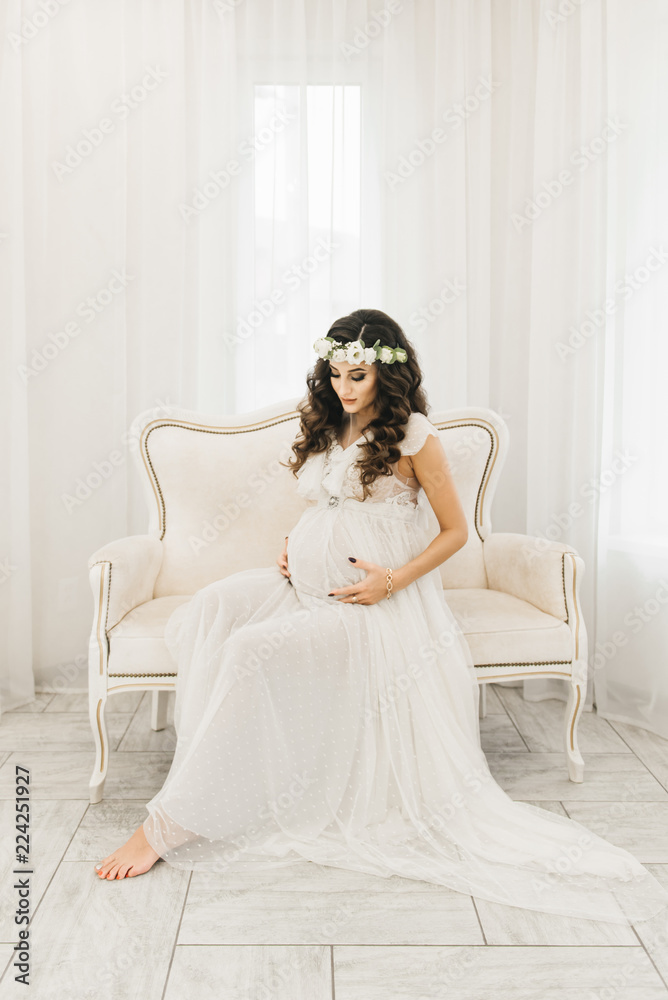 Attractive young pregnant girl in white dress with curls. Photo session waiting for the baby Attractive young pregnant girl in white dress with curls. Photo session waiting for the baby