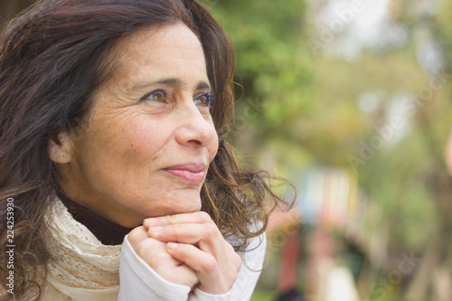 Middle aged nice lady with optimistic look resting face on her hands in the park. Visionary woman, entrepreneur imagination, pensive, freedom, retirement planning concepts
