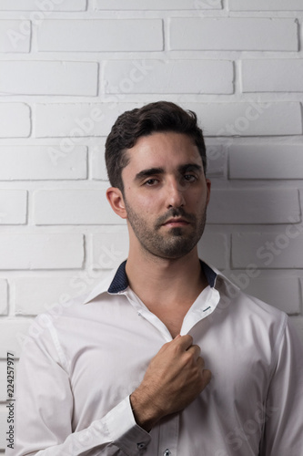 young white man wearing social outfit standing and posing in front of white brick wall photo