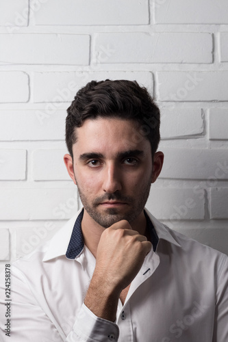 young white man wearing social outfit standing and posing in front of white brick wall photo