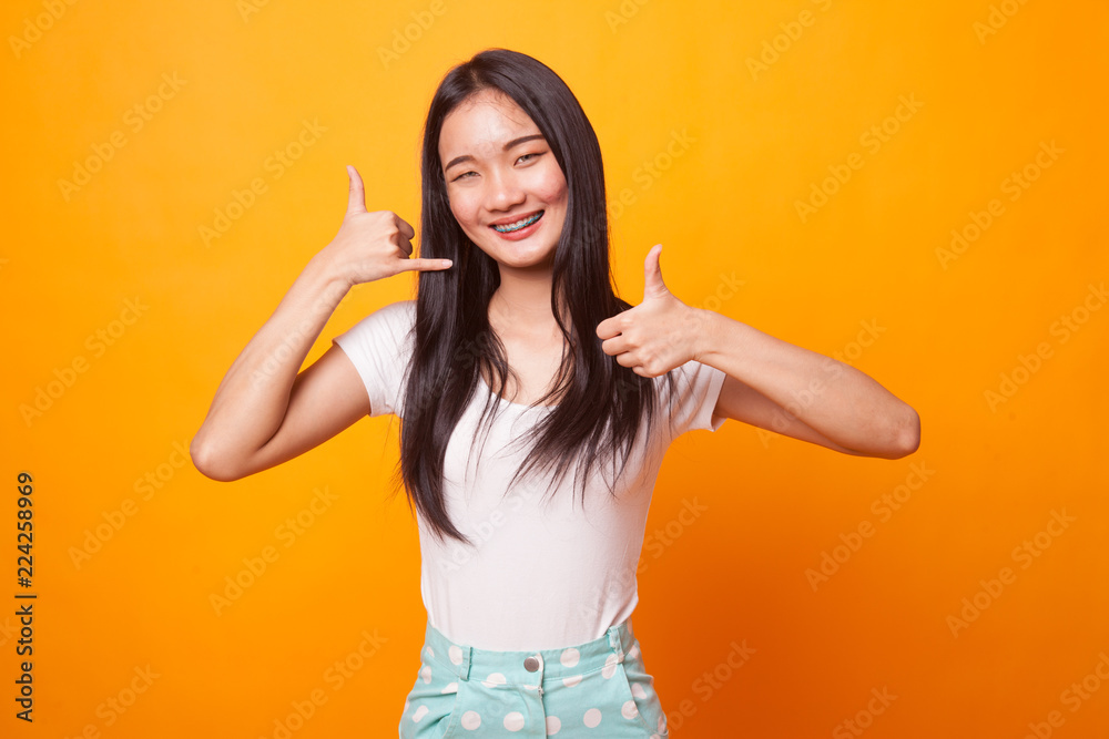 Young Asian woman thumbs up show with phone gesture. Young Asian woman thumbs up show with phone gesture.
