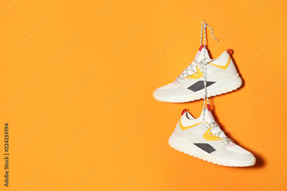 Pair of stylish sneakers hanging on color wall, space for text - obrazy, fototapety, plakaty 