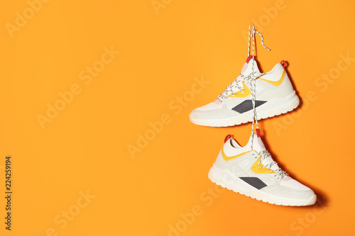 Pair of stylish sneakers hanging on color wall, space for text