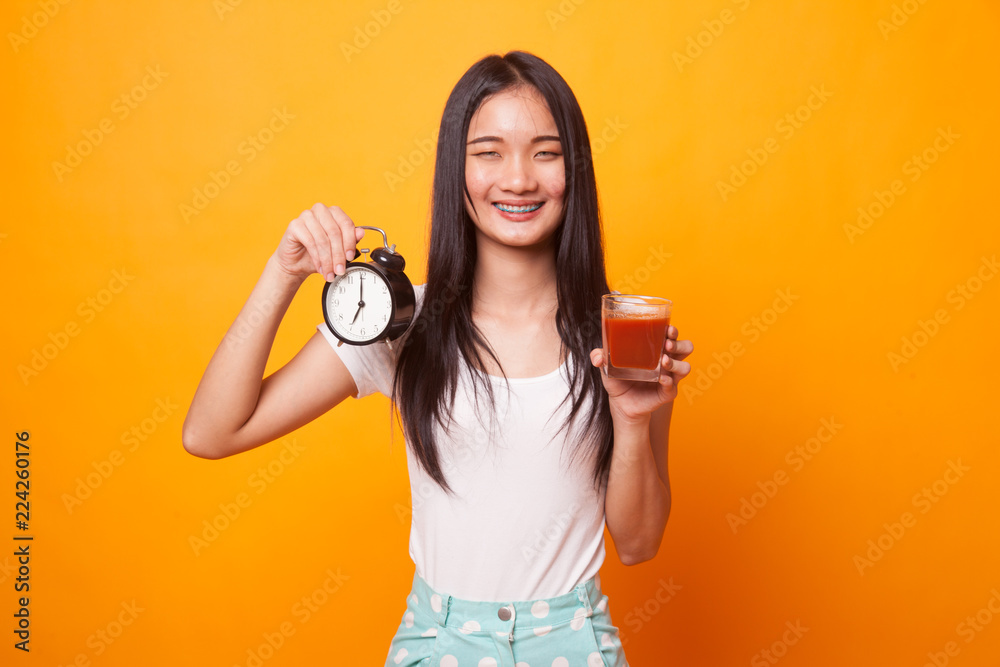 Young Asian woman with tomato juice and clock. Young Asian woman with tomato juice and clock.