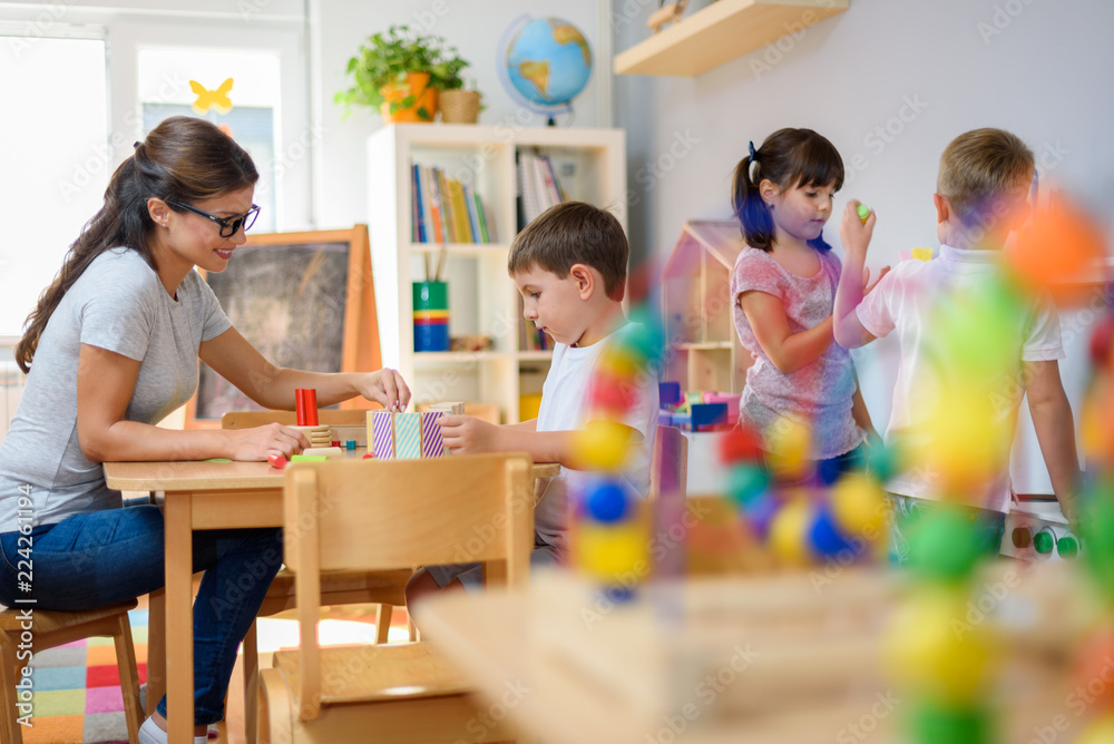 Preschool teacher with children playing with colorful wooden didactic toys at kindergarten - obrazy, fototapety, plakaty 