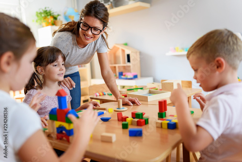 Photo Preschool teacher with children playing with colorful wooden didactic toys at ki
