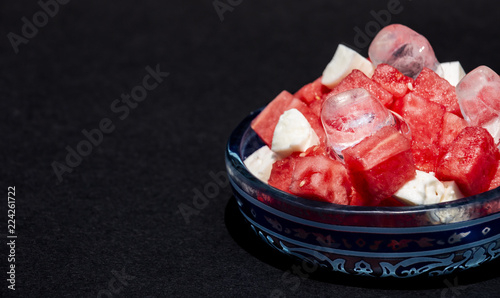 Summer salad watermelon with feta cheese and ice on a black background