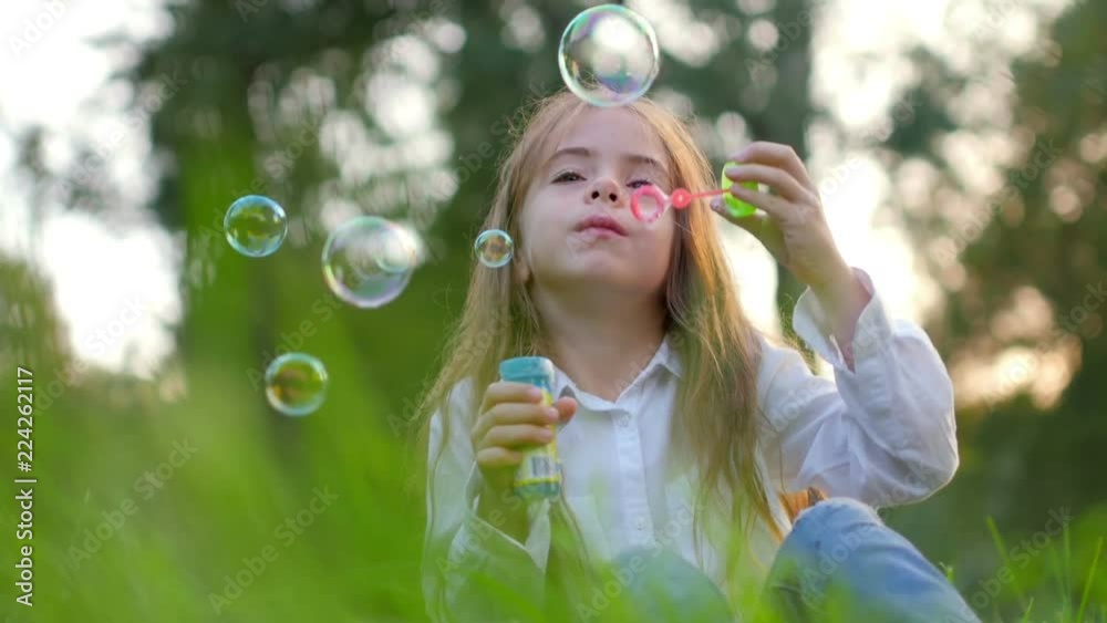 Beautiful girl sitting on the grass in the park lets bubbles, children's games Beautiful girl sitting on the grass in the park lets bubbles, children's games