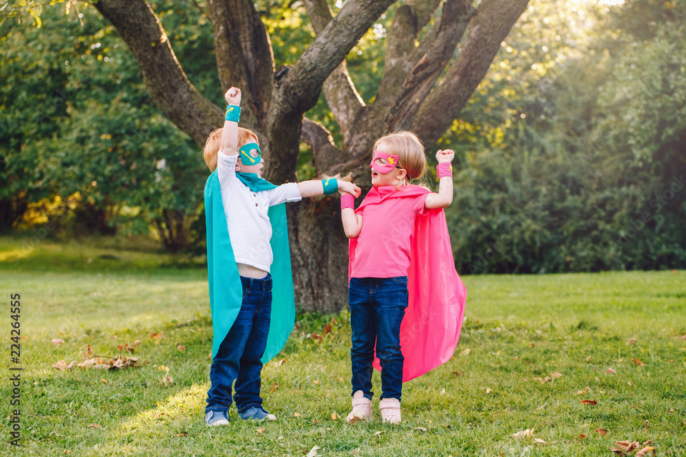 Fototapeta premium Cute adorable preschool Caucasian children playing superheroes. Two kids friends having fun together outdoors in park. Happy active childhood and friendship concept. Creativity and power.