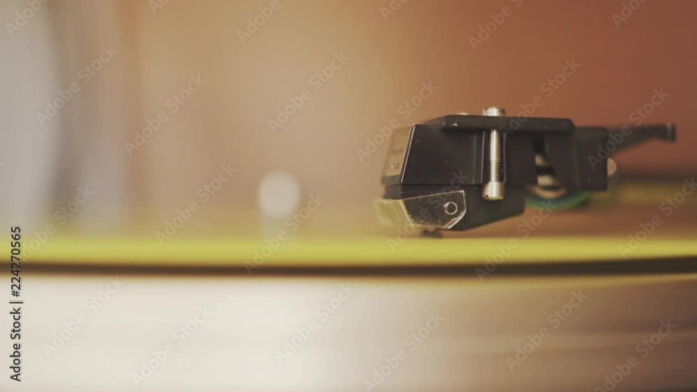 Close up shot of a record player from the 1970's. The needle is on a yellow vinyl record, playing at 33 1/3 rpm. The record player is in a cabinet.