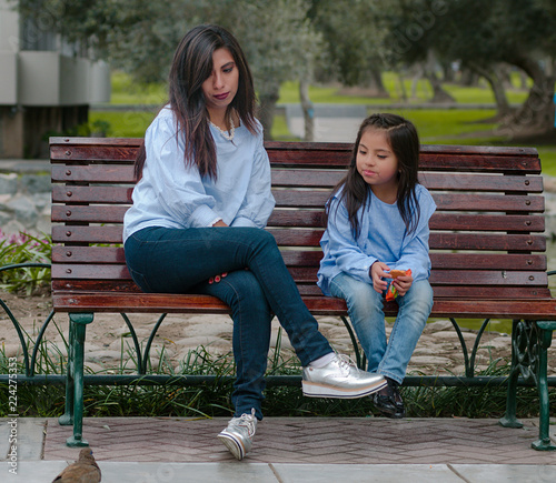 Mother and her little daughter sitting on a bench in the park