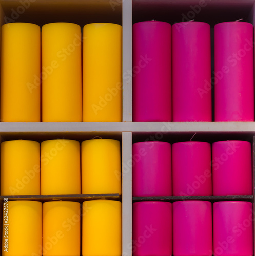Purple, pink, yellow small and large candles stacked on a shelf