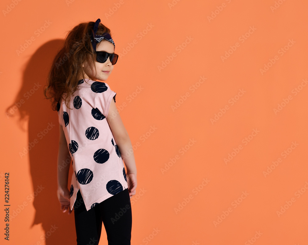 Five years old girl kid posing in summer shirt and sunglasses on orange background