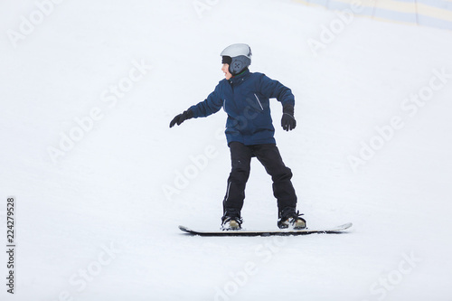 cute young boy, brave kid in gray helmet and orange googles, in blue jacket snowboarding on white snow mountain. winter sport, active lifestyle concept