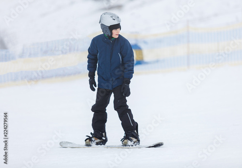 cute young boy, brave kid in gray helmet and orange googles, in blue jacket snowboarding on white snow mountain. winter sport, active lifestyle concept © Natali