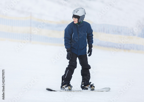 cute young boy, brave kid in gray helmet and orange googles, in blue jacket snowboarding on white snow mountain. winter sport, active lifestyle concept © Natali