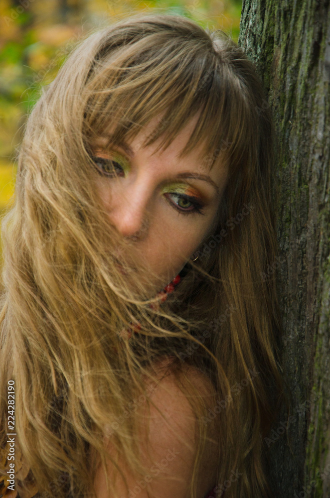 young woman in the woods leaning against the trunk of an old tree young woman in the woods leaning against the trunk of an old tree