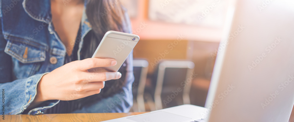 Woman hand uses a smartphone and works in a laptop at offices.Web banner.