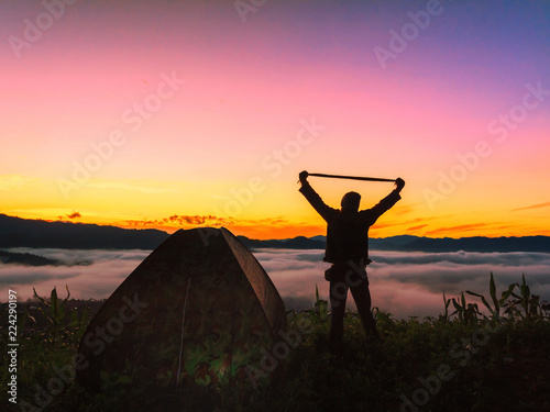 Silhouette of happy man standing with near a camping tent at sunrise ,success concept.