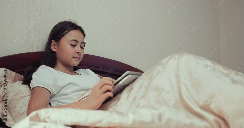 Cute little girl lies with a tablet computer on her bed in the evening Cute little girl lies with a tablet computer on her bed in the evening