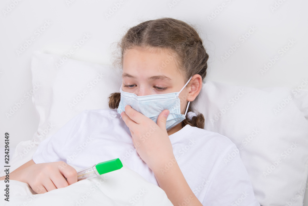 a girl who is sick and lies in bed in a gauze dressing, holds a thermometer in her hand, to measure temperature