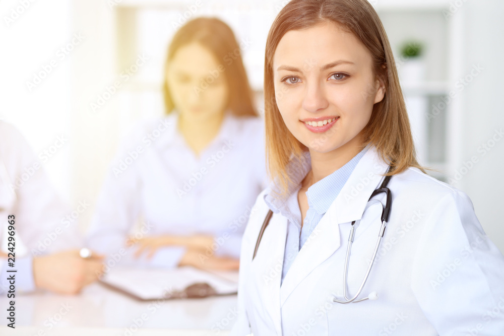 Young beautiful female doctor smiling on the background with patient in hospital Young beautiful female doctor smiling on the background with patient in hospital