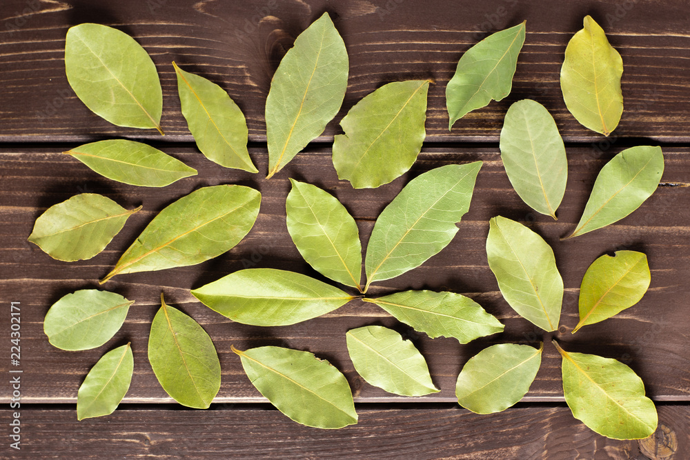 Lot of whole dry olive green bay laurel leaves flatlay on brown wood Lot of whole dry olive green bay laurel leaves flatlay on brown wood