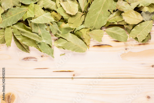 Lot of whole dry olive green bay laurel leaves above flatlay on natural wood photo