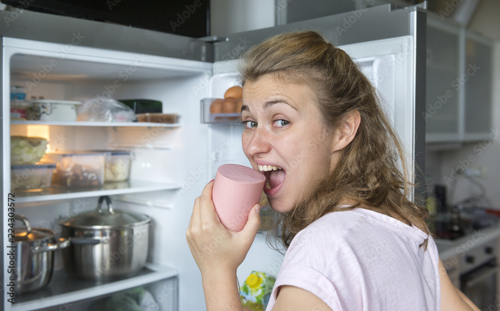 girl biting a sausage in front of the fridge
