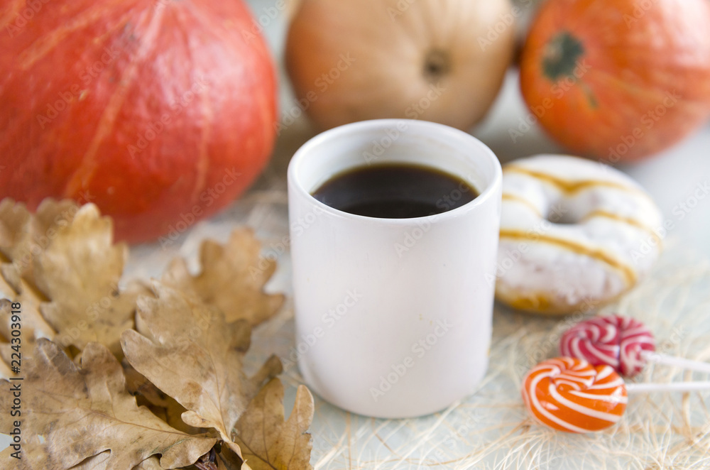 1 white Cup of coffee among pumpkins, one Donat with icing, lollipops, dry oak leaves