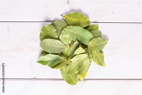 Lot of whole dry olive green bay laurel leaves stack flatlay on white wood photo