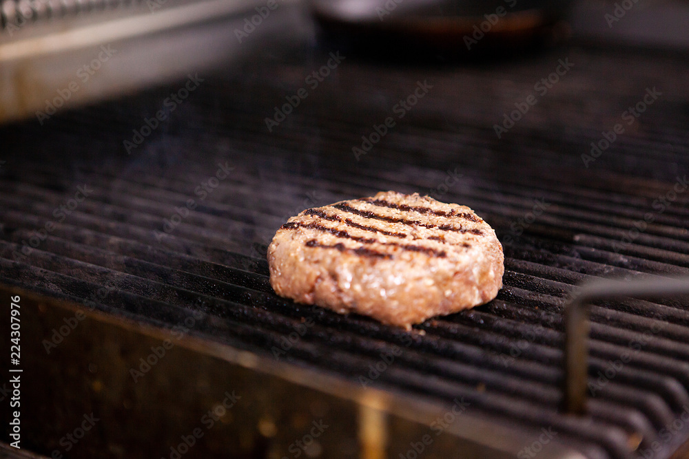 Chef is grilling a meat burger on the grill. Fast cuisine