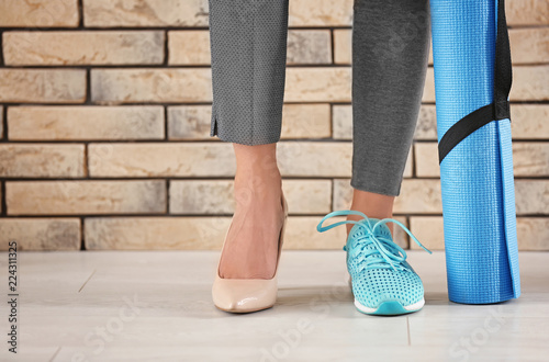 Young woman wearing high-heeled shoe and sneaker near brick wall. Concept of balance between rest and work