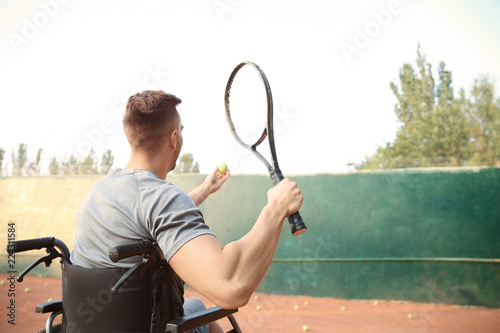 Young man in wheelchair playing tennis on court photo