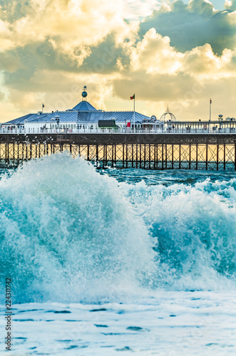 Brighton Pier, Brighton, Sussex, Britain on a stormy evening at dusk as the sun is setting. There are high waves and surf on the beach