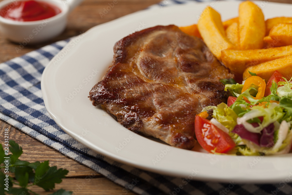 Grilled pork neck served with French fries and salad. Grilled pork neck served with French fries and salad.