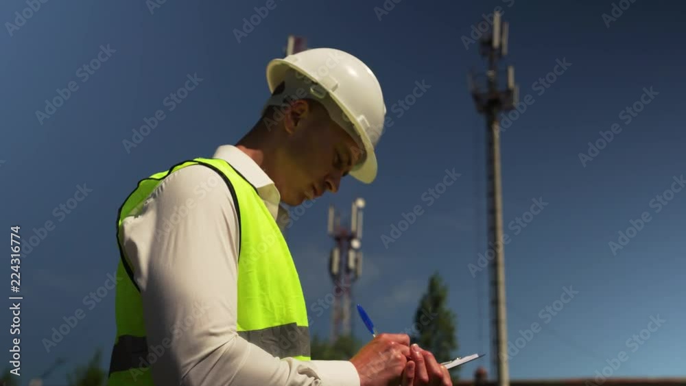 Young Male Chief Engineer In Helmet And Green Waistcoat Inspects A New Power Plant Located Outside The City Signing Documents On The Successful Delivery Of The Facility Young Male Chief Engineer In Helmet And Green Waistcoat Inspects A New Power Plant Located Outside The City Signing Documents On The Successful Delivery Of The Facility
