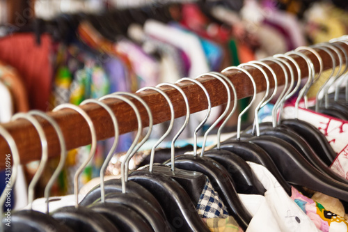 Wooden clothes racks with hangers and with colorful clothes on a blurred background inside shop.