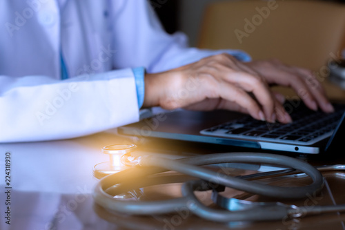 Slika na platnu Female doctor hands typing on laptop computer keyboard with medical stethoscope on the desk