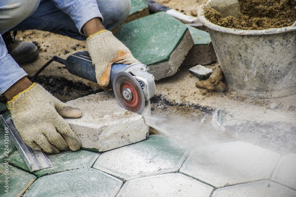 The workers cutting green concrete hexagonal blocks for paving.