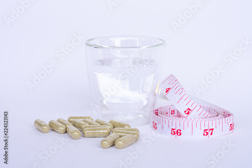 Capsule of medicine, glass of water and measuring tape isolated on white background. Take medicine, drug for on diet in concept. photo