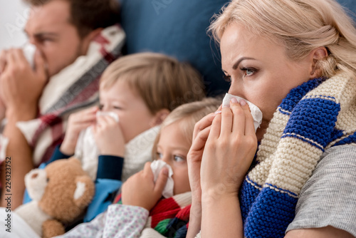 close-up shot of sick young family blowing noses with napkins together while lying in bed