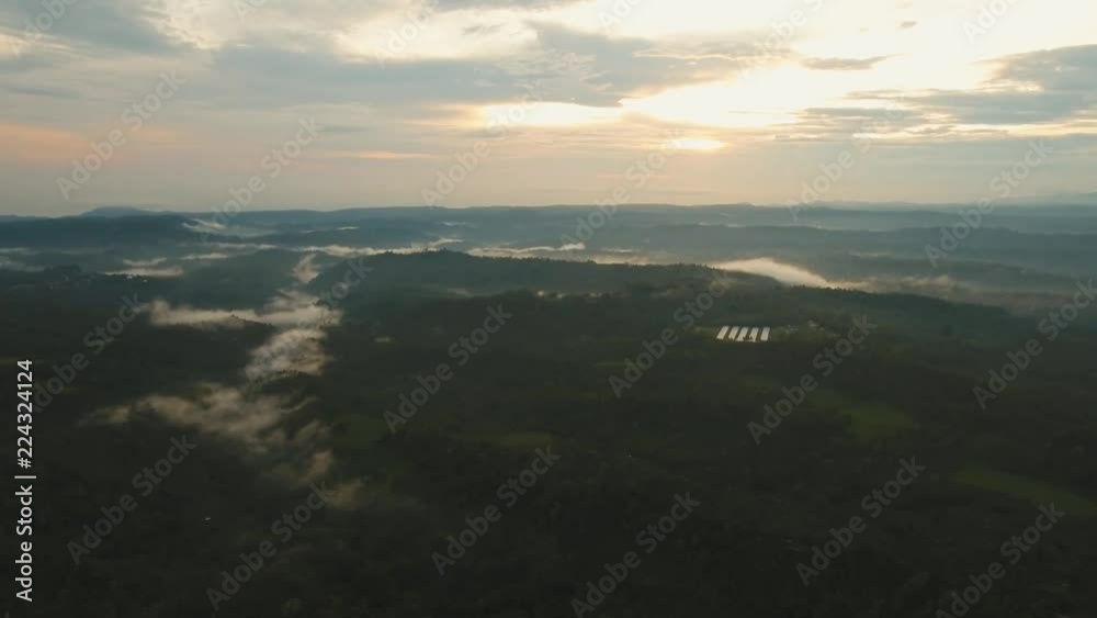 Aerial view of forest, farmland, fields, mountains with fog, clouds at sunset on Bali,Indonesia. Sunset landscape on a tropical island. Travel concept. Aerial footage.