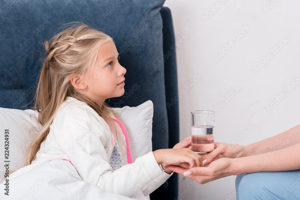 cropped shot of mother giving pills and water to her diseased daughter cropped shot of mother giving pills and water to her diseased daughter