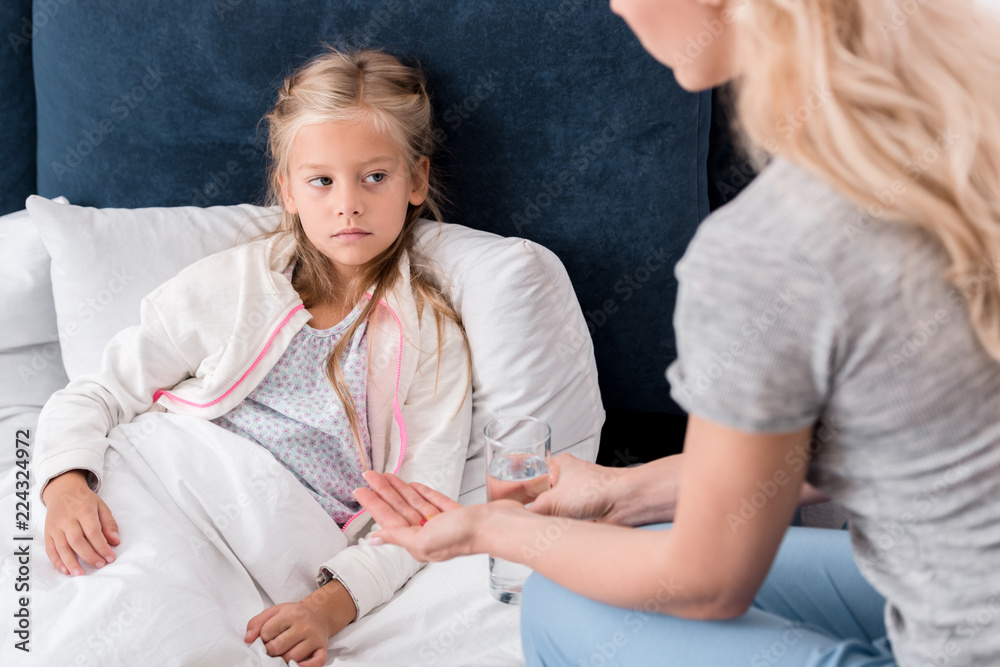 Obraz premium cropped shot of mother giving pills and water to her ill daughter in bed