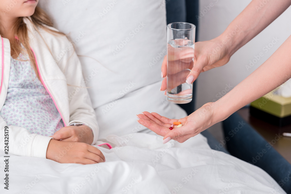 Fototapeta premium cropped shot of mother giving pills and water to her sick daughter in bed