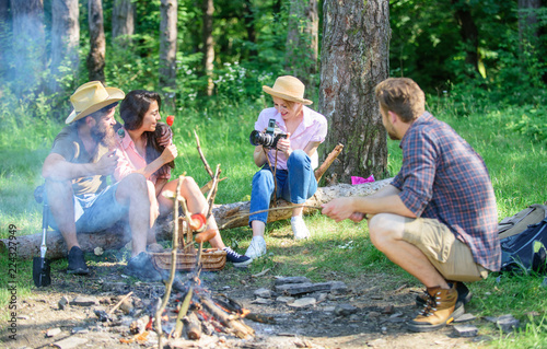 Company having hike picnic nature background. Tourists sharing thoughts about hike sit on log. Picnic with friends in forest near bonfire. Hikers sharing impression of walk forest. Summer tradition